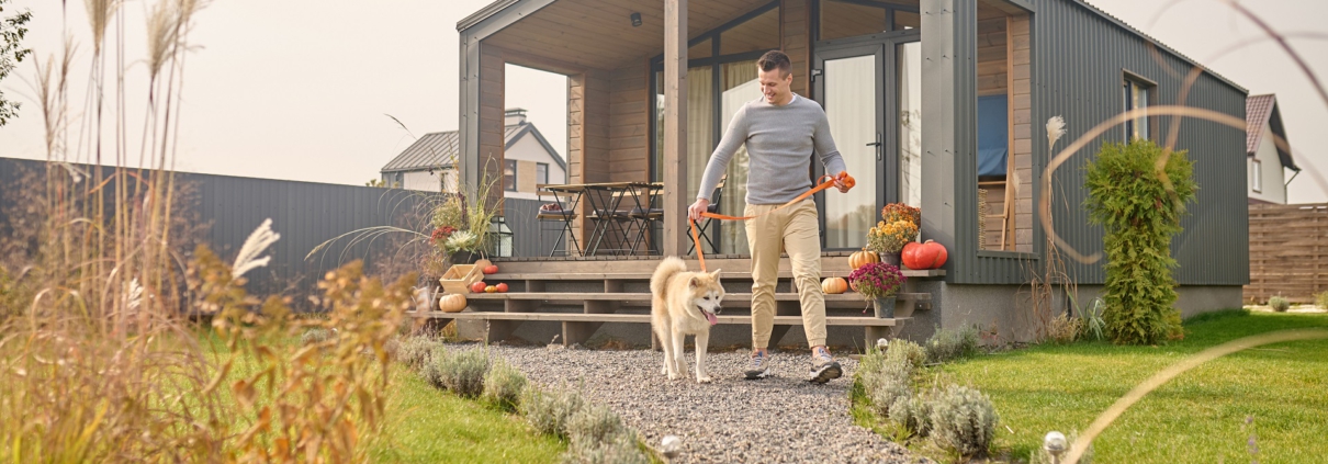 Ein Mann verlässt mit seinem weißen Hund das Haus über den Garten.