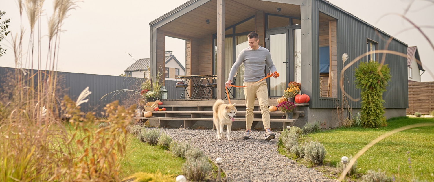 Ein Mann verlässt mit seinem weißen Hund das Haus über den Garten.