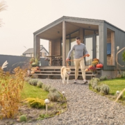 Ein Mann verlässt mit seinem weißen Hund das Haus über den Garten.