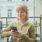 Eine junge Frau sitzt auf dem Balkon und tippt auf ihrem Handy.