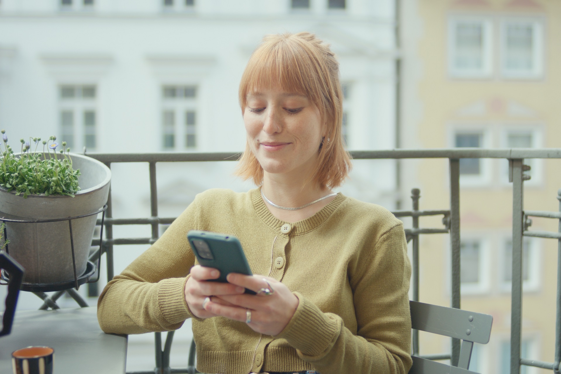 Eine junge Frau sitzt auf dem Balkon und tippt auf ihrem Handy. Eine junge Frau sitzt auf dem Balkon und tippt auf ihrem Handy.