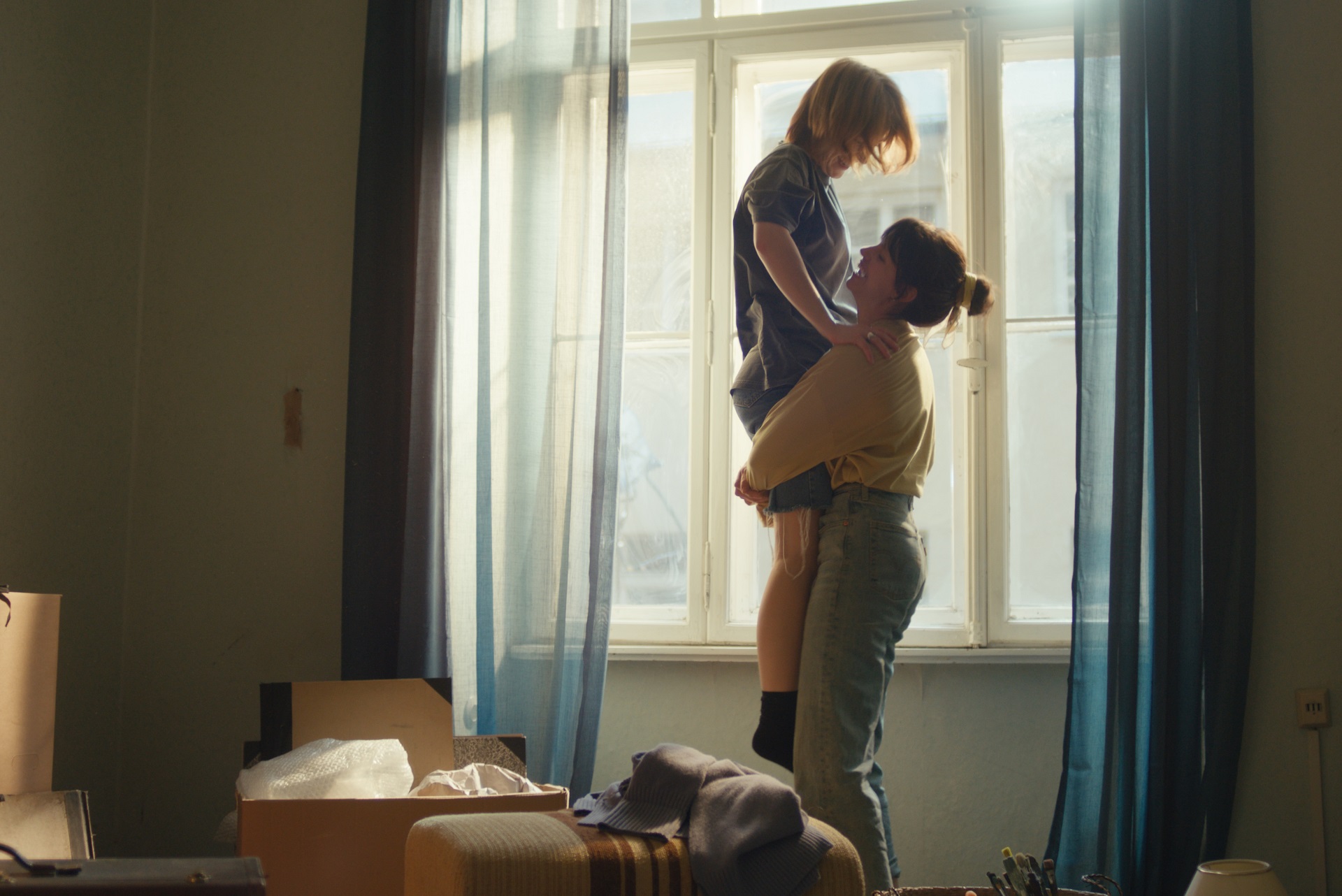 Zwei junge Frauen stehen in einer Wohnung mit Umzugskartons vor dem Fenster. Die eine hebt die andere voller Freude hoch. Zwei junge Frauen stehen in einer Wohnung mit Umzugskartons vor dem Fenster. Die eine hebt die andere voller Freude hoch.