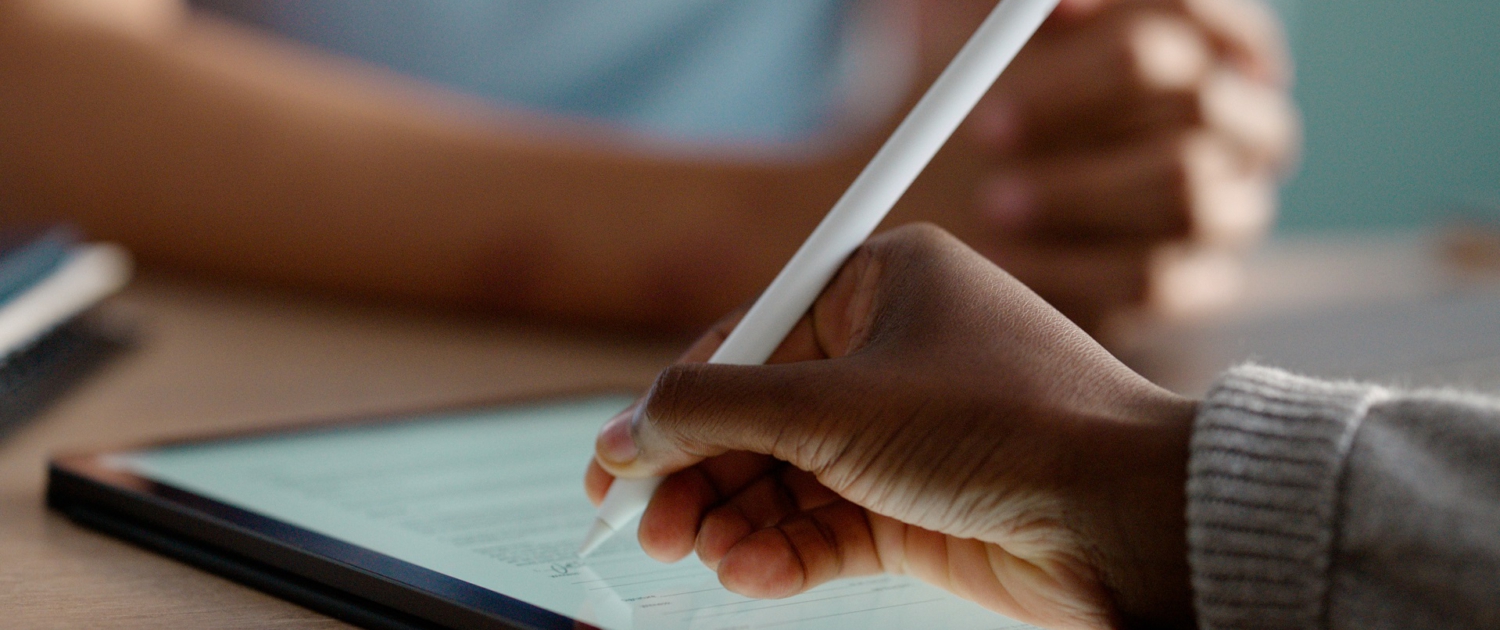Im Fokus liegt ein Tablet auf einem Tisch. Eine Hand hält einen Stift und unterschreibt ein digitales Formular auf dem Bildschirm. Im Fokus liegt ein Tablet auf einem Tisch. Eine Hand hält einen Stift und unterschreibt ein digitales Formular auf dem Bildschirm.
