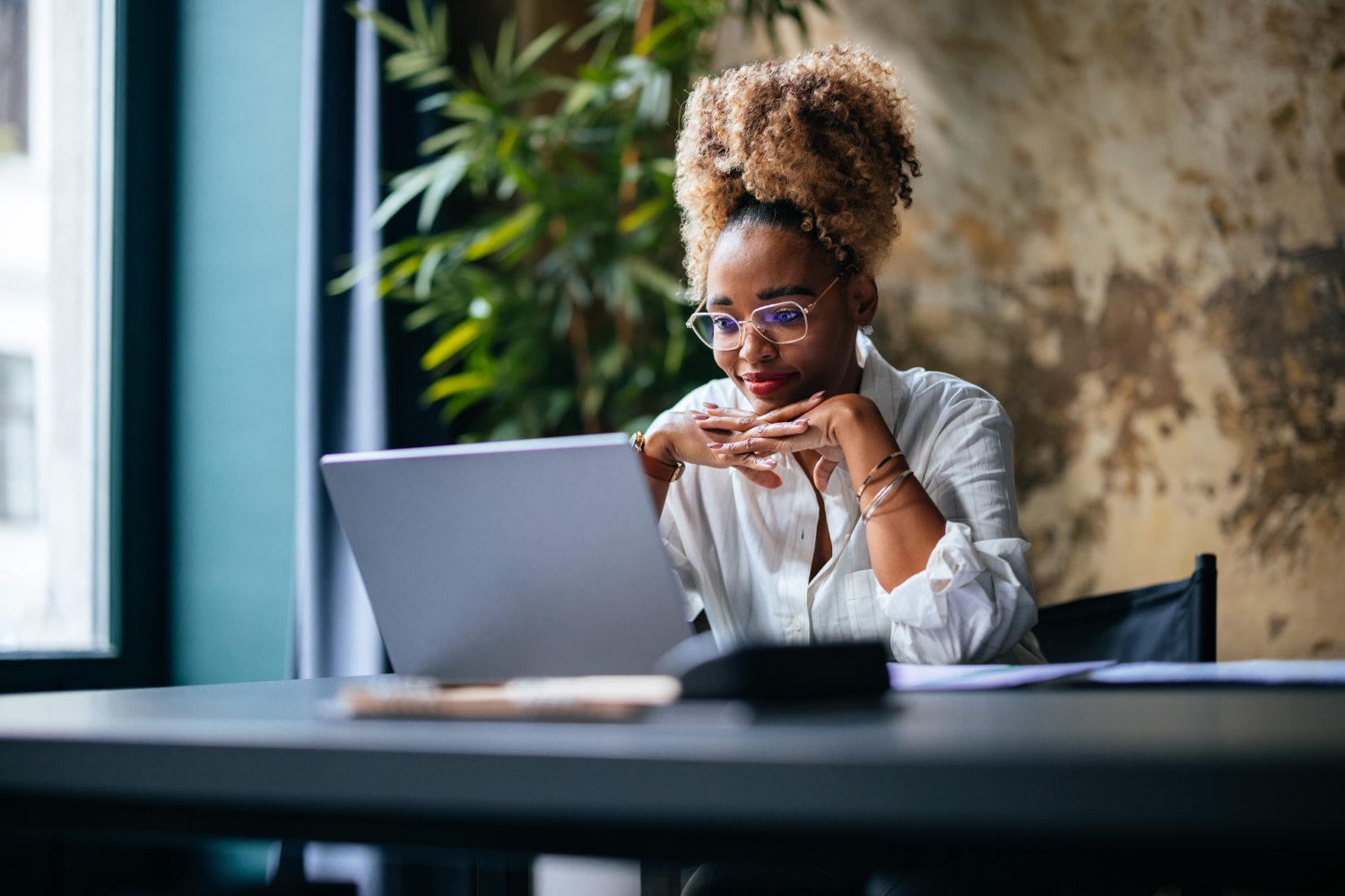 Eine dunkelhäutige Frau sitzt vor Ihrem Laptop in einem Büro. Sie blickt freundlich aber nachdenklich auf den Bildschirm. Eine dunkelhäutige Frau sitzt vor Ihrem Laptop in einem Büro. Sie blickt freundlich aber nachdenklich auf den Bildschirm.
