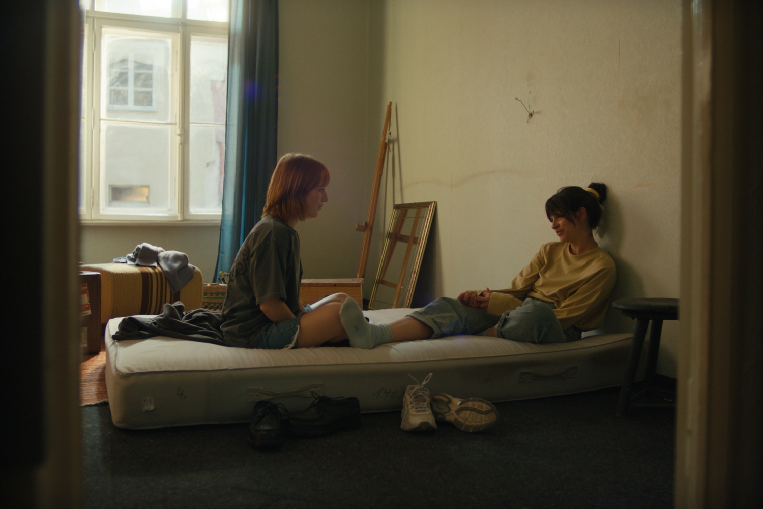 Zwei junge Frauen sitzen nach dem Umzug auf einer Matratze in einem noch unfertigen Zimmer.