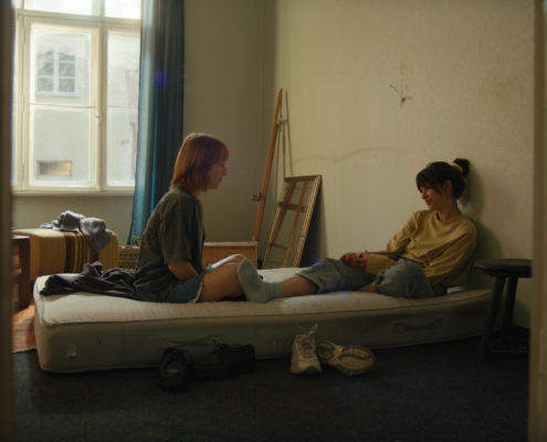 Zwei junge Frauen sitzen nach dem Umzug auf einer Matratze in einem noch unfertigen Zimmer.