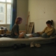 Zwei junge Frauen sitzen nach dem Umzug auf einer Matratze in einem noch unfertigen Zimmer.
