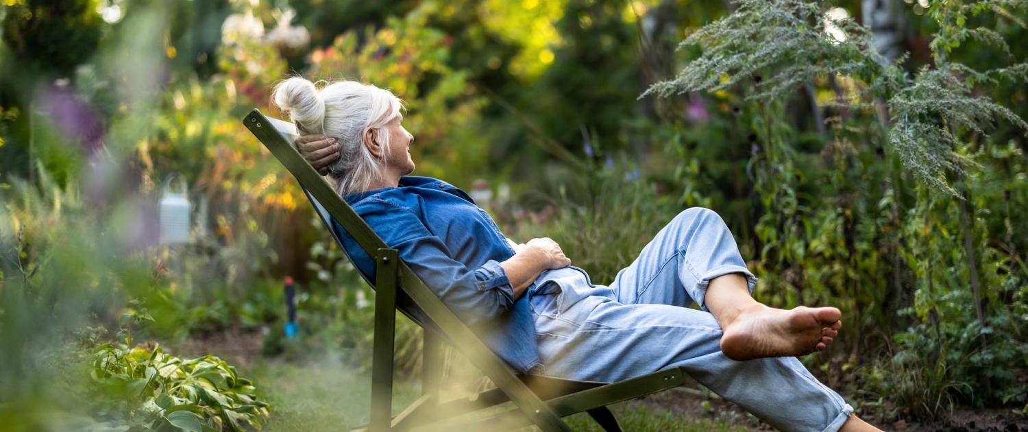 Eine ältere aber noch sehr fitte Frau sitzt in einem Liegestuhl mitten in einem grünen Garten. Sie blickt verträumt in die Ferne. Eine ältere aber noch sehr fitte Frau sitzt in einem Liegestuhl mitten in einem grünen Garten. Sie blickt verträumt in die Ferne.