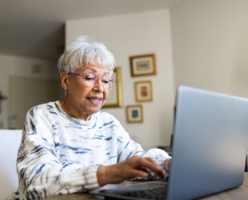 Eine ältere Frau sitzt zu Hause am Tisch und nutzt einen Laptop.