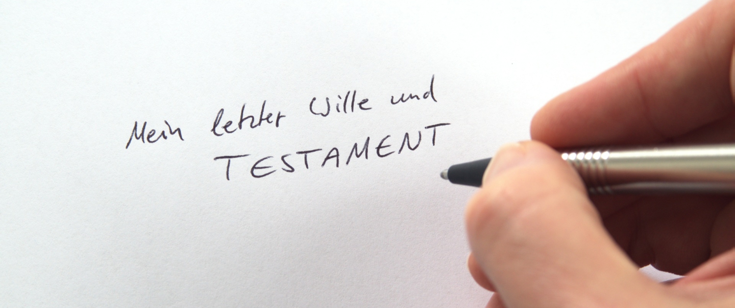 Hand schreibt „Mein letzter Wille und Testament“ auf ein Blatt Papier